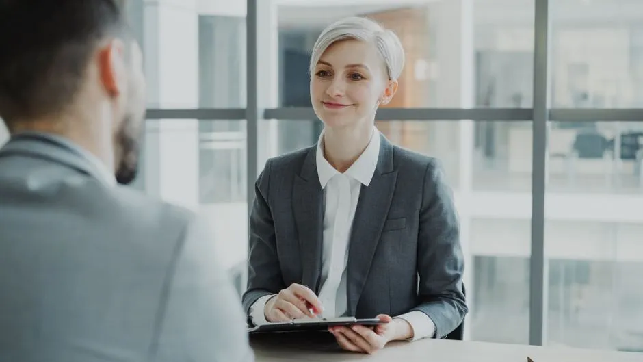 Two people talking across a table in a modern office, illustrating a job interview or HR meeting